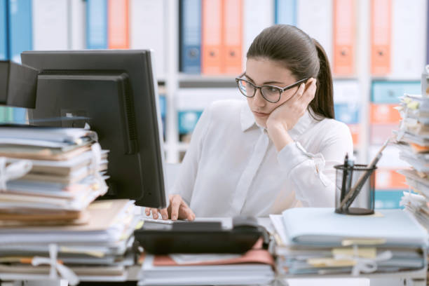 Young bored office worker sitting at desk and working, she is overloaded with paperwork