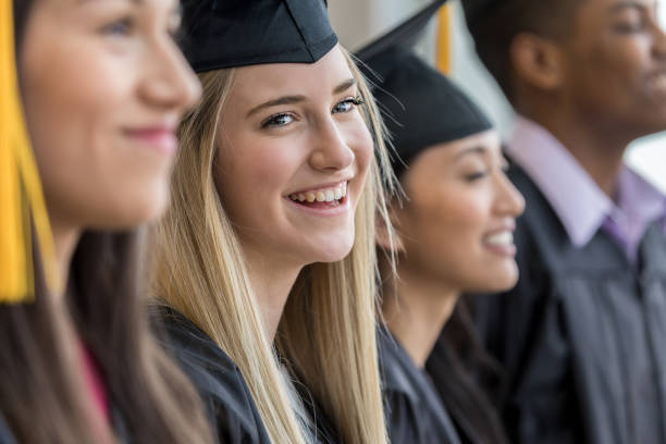 Standing with her fellow graduates, a teen girl smiles with joy at her parents.